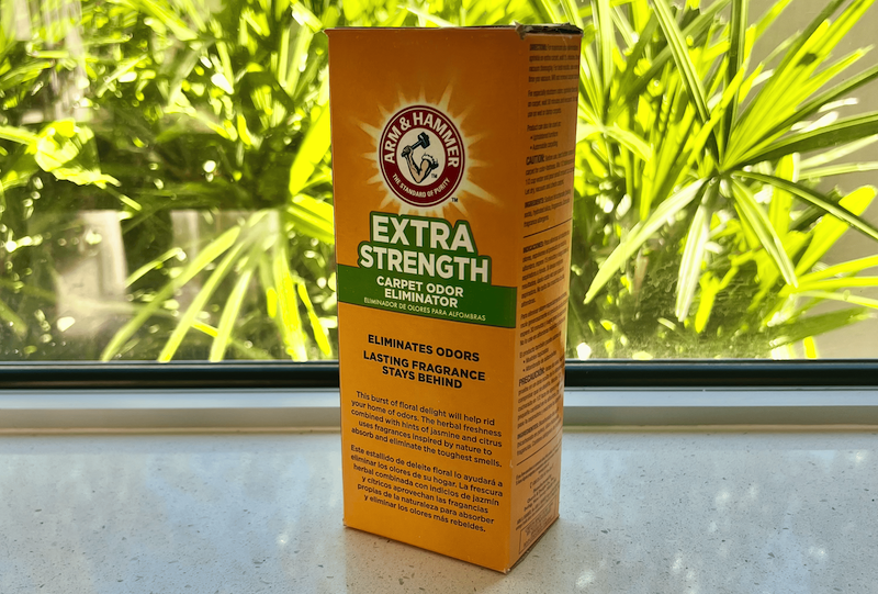 Box of Arm & Hammer Extra Strength Carpet Odor Eliminator sitting on a windowsill with green plants visible in the background. This baking soda-based deodorizer is highly recommended for eliminating persistent rug odors while being gentle on fibers. The formula features natural fragrances including jasmine and citrus to leave carpets smelling fresh. (arm-and-hammer-deodorizer