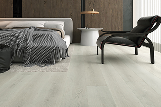 Minimalist bedroom interior featuring pale Eclipse Aqua Schild laminate flooring, upholstered low-profile bed, black lounge chair, white side table and dark wood feature wall.